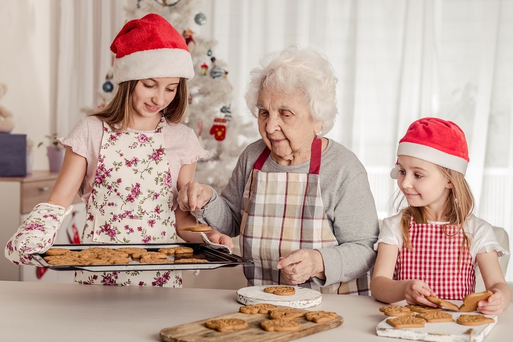 Grandmother,With,Granddaughters,In,Santa,Hats,Baking,Cookies