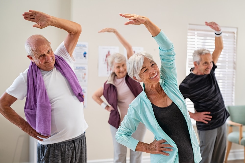 Group,Of,Seniors,Doing,Stretching,Exercise,Together,At,Retirement,Centre.