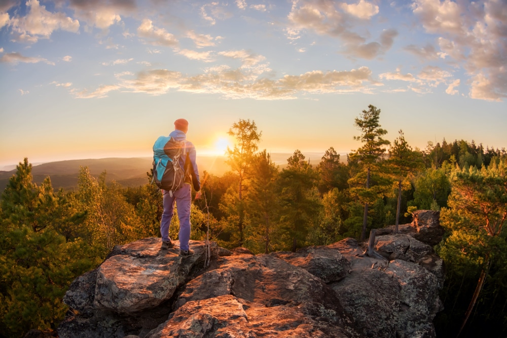 Hiker,With,Backpack,Standing,On,A,Rock,And,Enjoying,Sunset